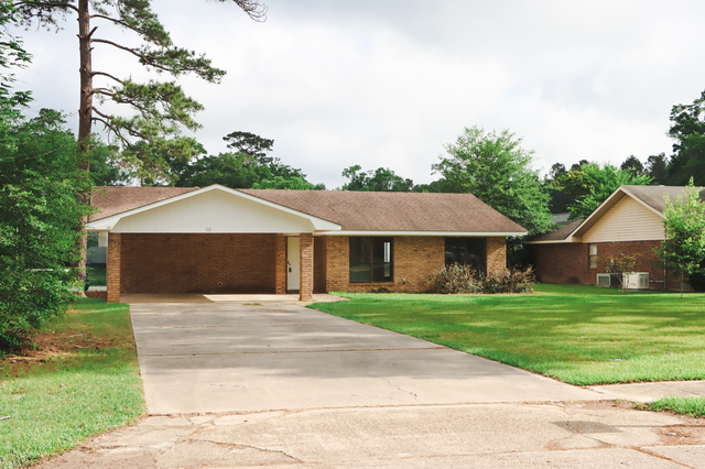 Front exterior of 1512 Lisa Lane Oakdale LA brick home with two-car carport and manicured lawn